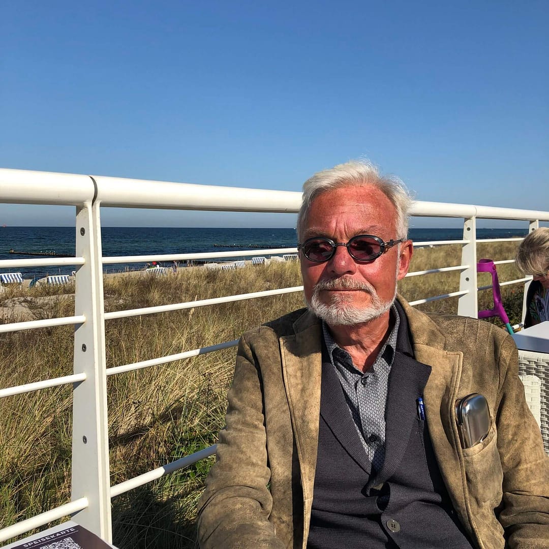Älterer Herr sitzt am Meer unter blauem Himmel