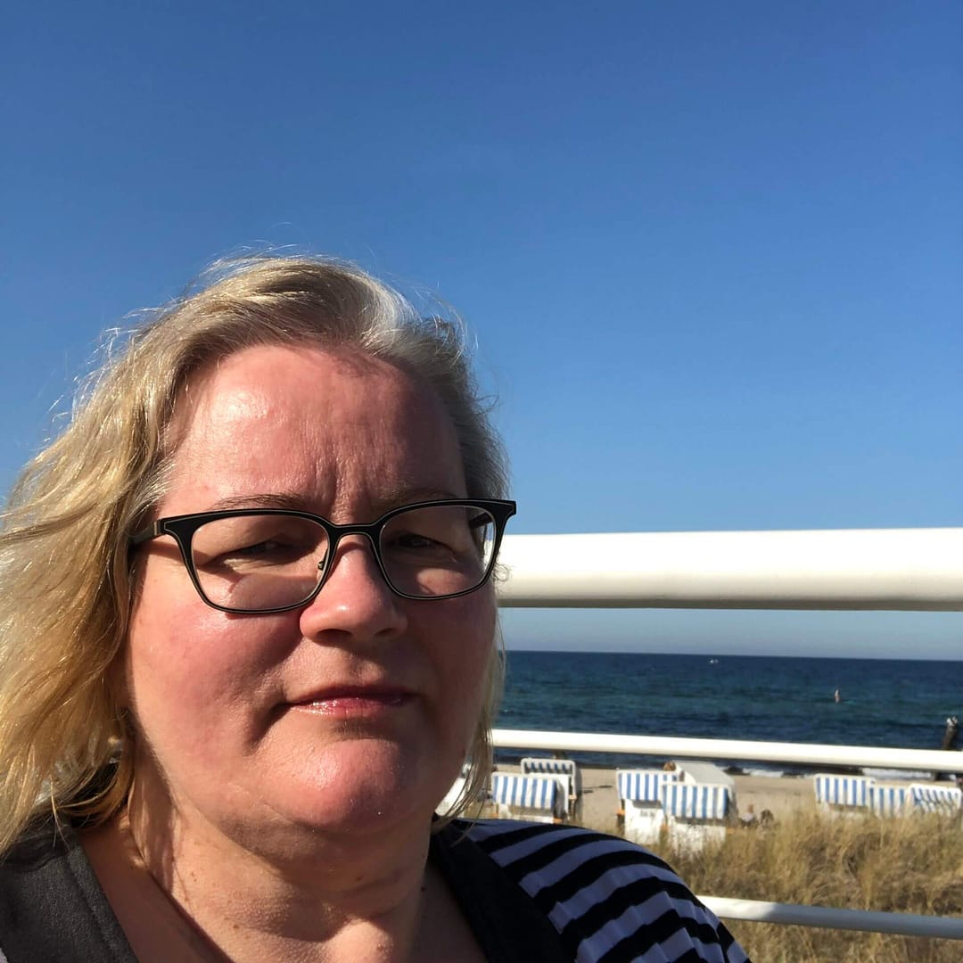 Frau vor Meer mit Brille und Strandkörben.