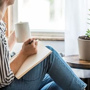 birgit-nora-schaefer-persoenlichkeitsentwicklung-frau-beim-journalling-1000x1000 Frau sitzt mit einem Kaffeebecher und einem Block auf dem Schoss beim Journalling zum Thema Persoenlichkeitsentwicklung