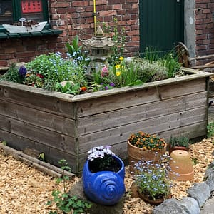 Vorgartenidylle mit Hochbeet voll blühender Blumen und blauem Keramiktopf