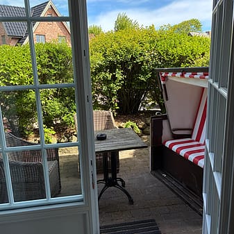 Geöffnete Terrassentür zu einem gemütlichen Garten mit Strandkorb