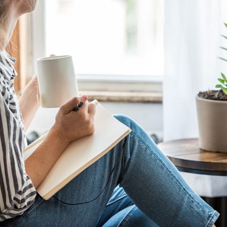 birgit-nora-schaefer-persoenlichkeitsentwicklung-frau-beim-journalling-1000x1000 Frau sitzt mit einem Kaffeebecher und einem Block auf dem Schoss beim Journalling zum Thema Persoenlichkeitsentwicklung