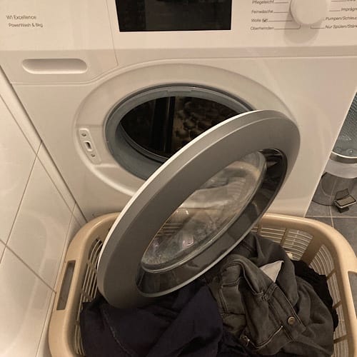 Offene Waschmaschine mit Kleidung im Korb