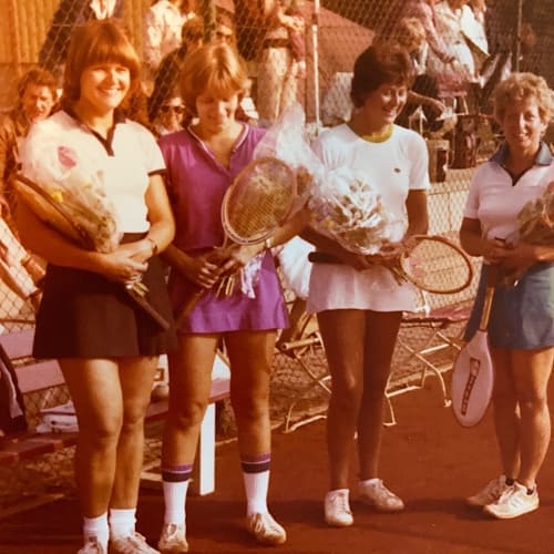 Vier Tennisspielerinnen mit Trophäen auf einem Platz