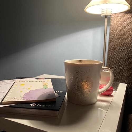 Tasse Kaffee neben Büchern auf Nachttisch mit Lampe