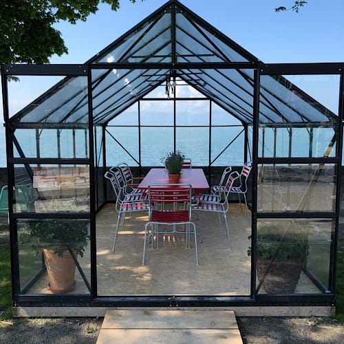 Glashaus mit Tisch und Stühlen am See