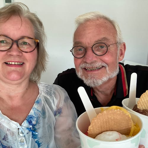 Birgit und Jürgen Schäfer genießen jeweils einen Eisbecher im Krankenhaus und lächeln dabei fröhlich