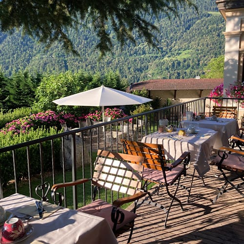 Terrasse von Schloß Plars, Algund, Südtirol, im morgendlichen Sonnenschein mit Blick auf die Berge und gedeckte Frühstückstische