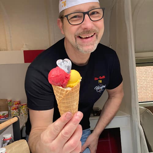 Freundlich lächelnder Eismann bietet mir eine Eiswaffel mit Mango- und Himbeereis an