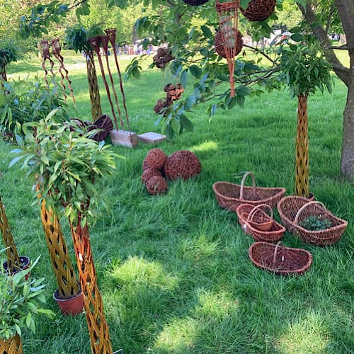 Vielfältige Korbwaren in einem Baum und auf der Wiese drapiert beim Kunsthandwerkermarkt im sonnigen Westfalenpark in Dortmund